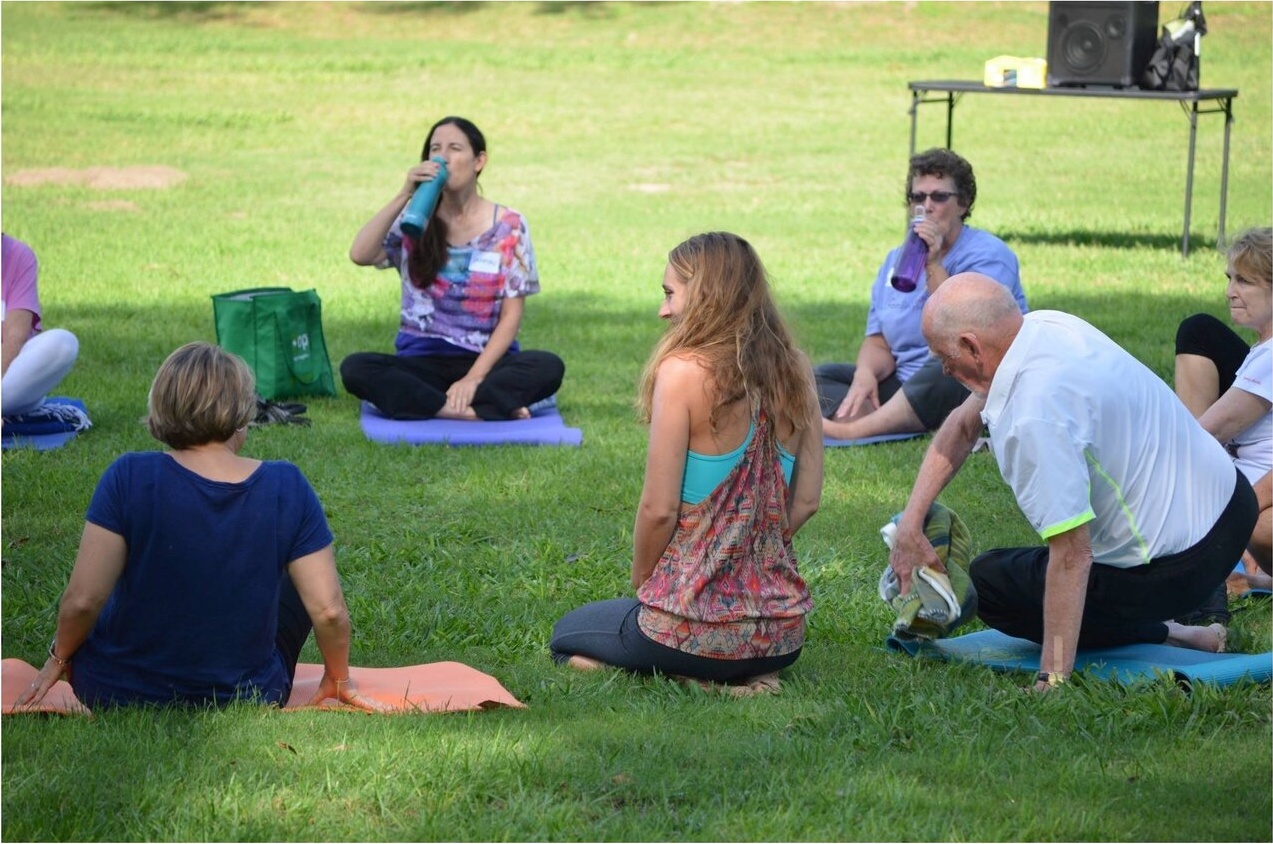 A small group practicing yoga together on the grass in a park