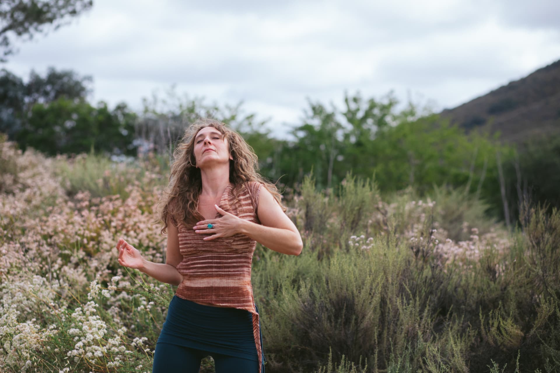 Jennica standing among wildflowers with one hand on her chest and eyes gently closed